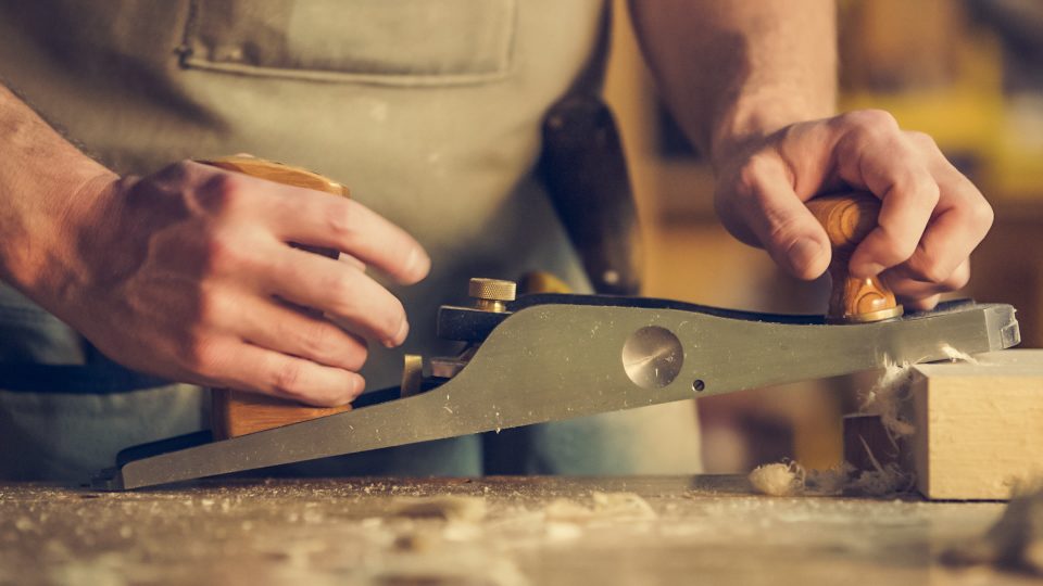 Hände eines Handwerkers beim Hobeln